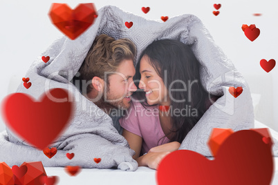 Composite image of attractive couple wrapped in the duvet