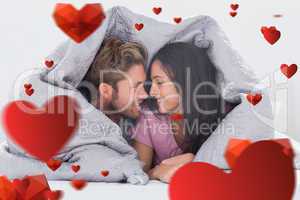 Composite image of attractive couple wrapped in the duvet