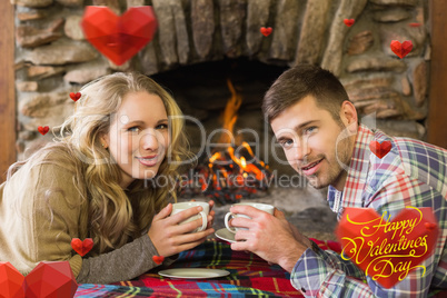 Composite image of couple with tea cups in front of lit fireplac