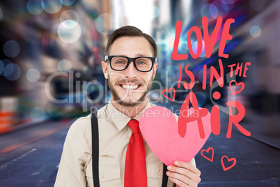 Composite image of geeky hipster smiling and holding heart card
