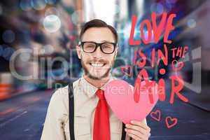 Composite image of geeky hipster smiling and holding heart card