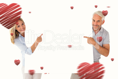 Composite image of happy couple holding and pointing to large po