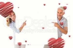 Composite image of happy couple holding and pointing to large po
