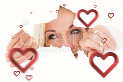 Composite image of blonde woman looking through torn paper