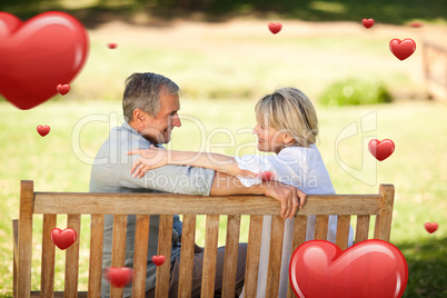 Composite image of happy retired couple sitting on the bench