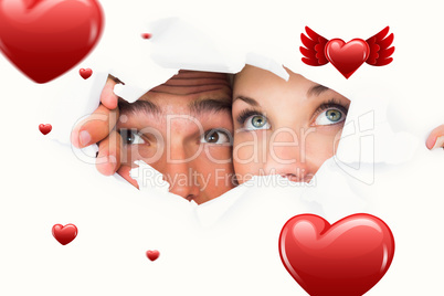 Composite image of young couple peeking through torn paper