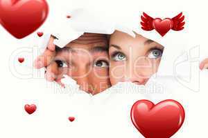 Composite image of young couple peeking through torn paper