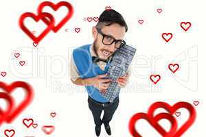 Composite image of geeky hipster looking at camera holding keybo