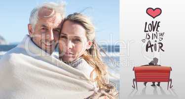 Composite image of smiling couple wrapped up in blanket on the b