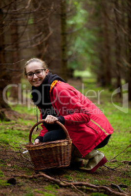 young woman collecting mushrooms in forest