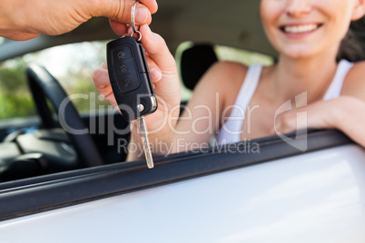 young smiling woman sitting in car taking key