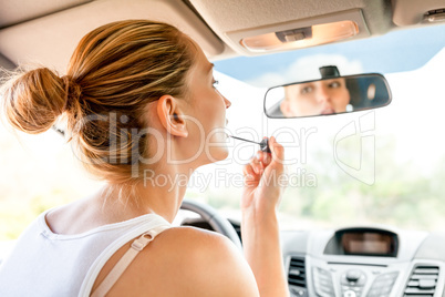 Beautiful woman applying makeup in the car