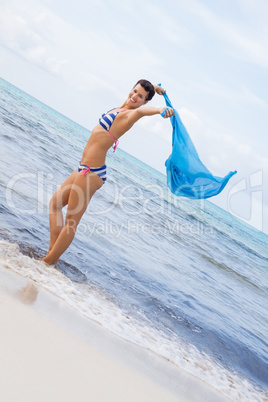 Carefree woman on a beach with a floating scarf