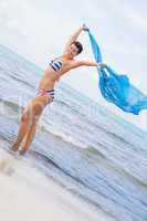 Carefree woman on a beach with a floating scarf