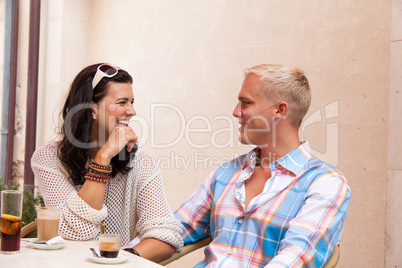 happy young couple sitting outside cafe restaurant drinking coffee
