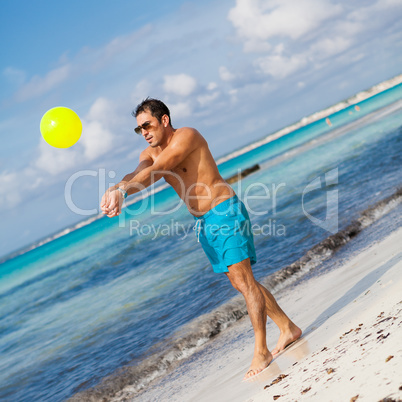 happy young adult man playing beach ball in summer
