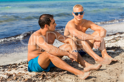 Two handsome young men chatting on a beach