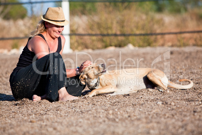 smiling blonde woman sitting outdoor with her dog