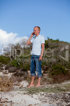 young man outside in summer on beach with mobile phone