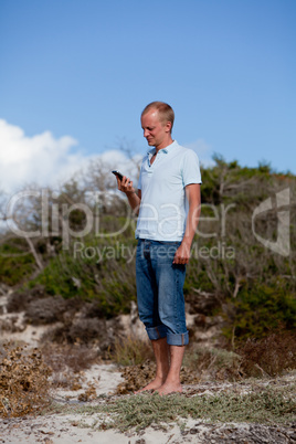 young man outside in summer on beach with mobile phone