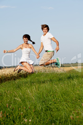 young happy couple jumping outside in summer