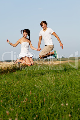 young happy couple jumping outside in summer