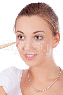 young beautiful woman applying concealer on face