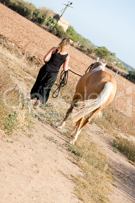 young woman walking a road with horse