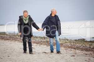 mature happy couple walking on beach in autumn