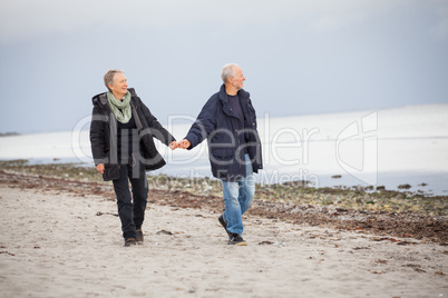 mature happy couple walking on beach in autumn