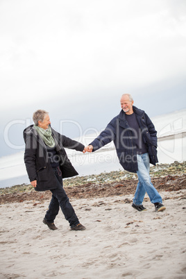 mature happy couple walking on beach in autumn