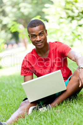 young smiling african student sitting in grass with notebook