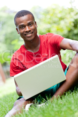 young smiling african student sitting in grass with notebook