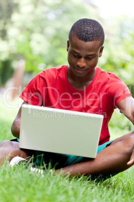 young smiling african student sitting in grass with notebook