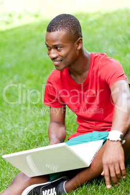 young smiling african student sitting in grass with notebook