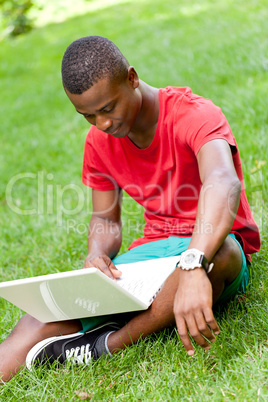 young smiling african student sitting in grass with notebook