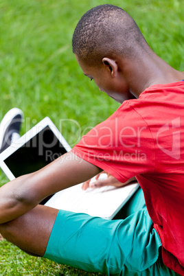 young smiling african student sitting in grass with notebook