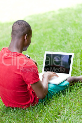 young smiling african student sitting in grass with notebook