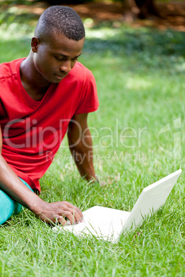 young smiling african student sitting in grass with notebook