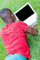 young smiling african student sitting in grass with notebook