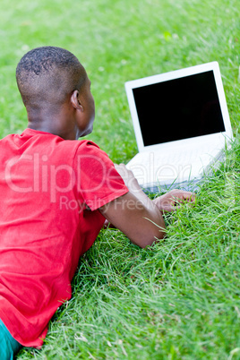 young smiling african student sitting in grass with notebook