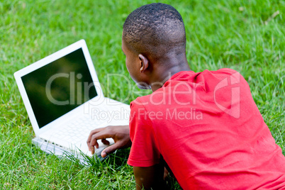 young smiling african student sitting in grass with notebook