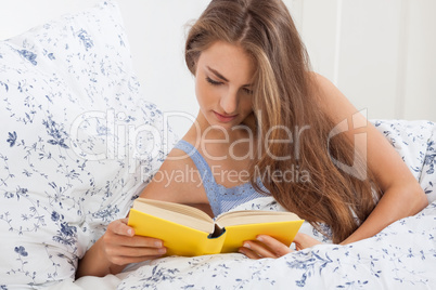 young attractive woman reading book lying in bed