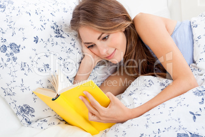young attractive woman reading book lying in bed