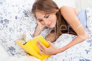 young attractive woman reading book lying in bed