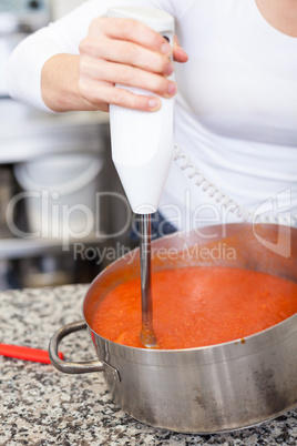 Woman chef whisking boiled tomato sauce in a pot