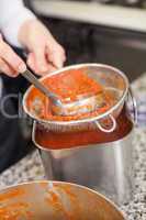 Woman chef whisking boiled tomato sauce in a pot