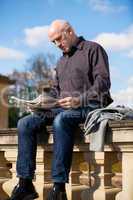 Man sitting reading a newspaper on a stone wall