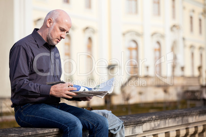 Man sitting reading a newspaper on a stone wall