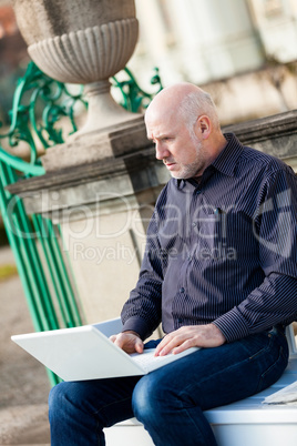 Man sitting on a bench using a laptop